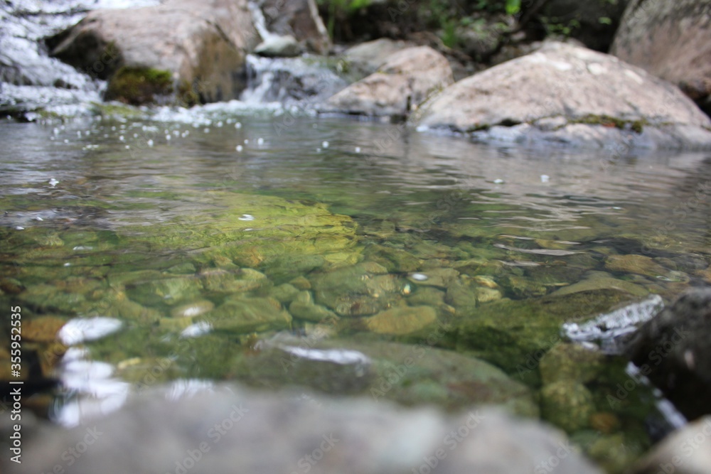 Mountain river - a small waterfall on a river with crystal clear water that flows among gray stones in a green forest on a cloudy summer day. Big stones near the pond Mountain river - a small waterfall on a river with crystal clear water that flows among gray stones in a green forest on a cloudy summer day. Big stones near the pond