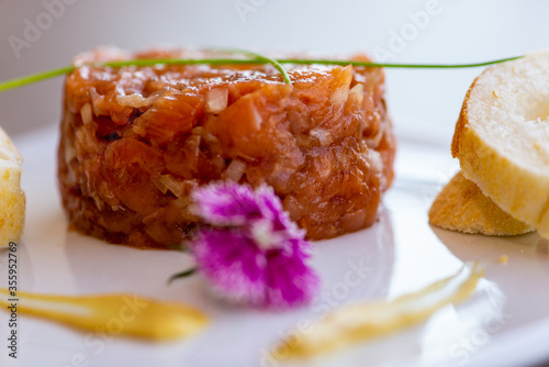 Homemade Salmon Tartare dish by amateur chef for culinary blogs, decorated with eatable purple flower and mostard. photo