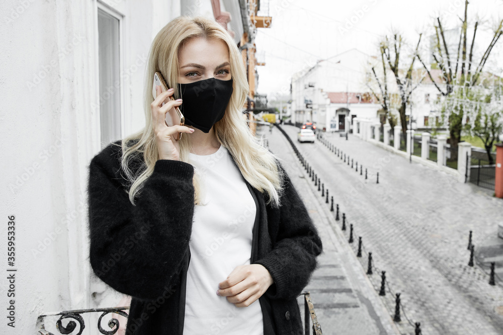 Fototapeta premium A girl in a black mask is standing on the balcony of the office and talking on the phone