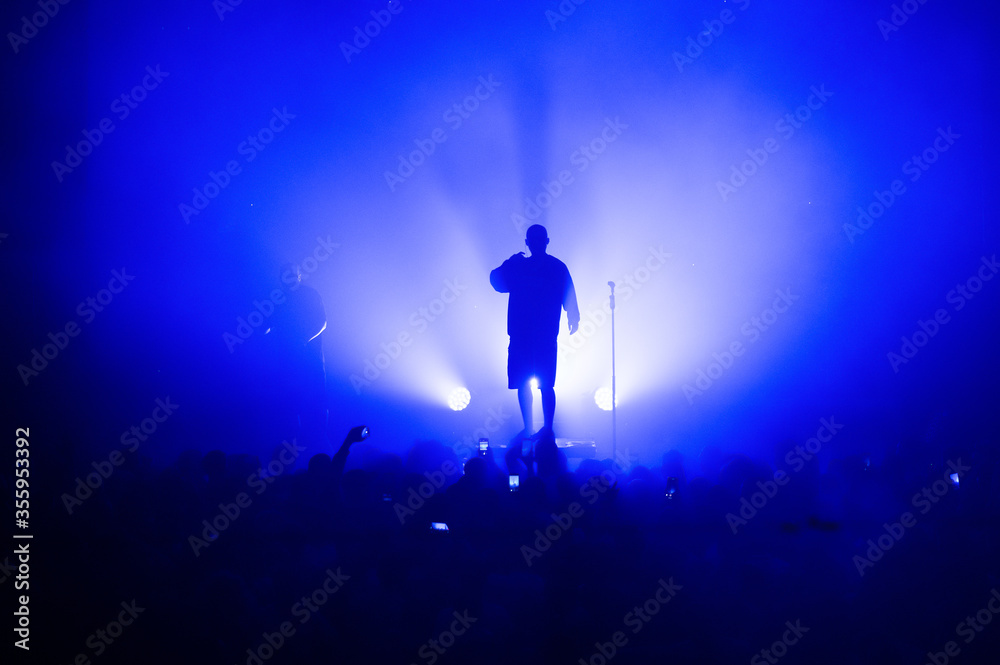 silhouette of a vocalist and microphone stand on stage in a blue haze. amazing show in the light of spotlights. concert for fans. poster