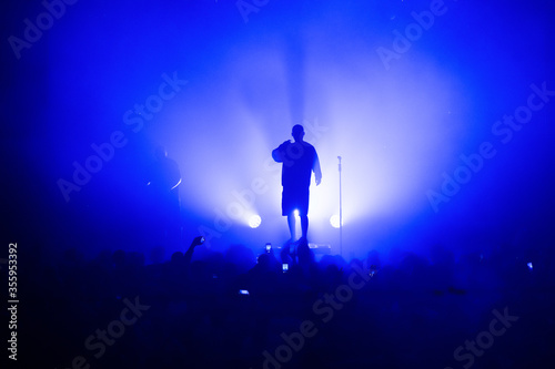 Obraz na płótnie silhouette of a vocalist and microphone stand on stage in a blue haze. amazing show in the light of spotlights. concert for fans. poster w salonie