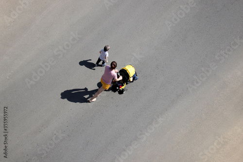 Fototapeta Naklejka Na Ścianę i Meble -  Woman with two kids crossing the street, top view. Concept of motherhood, road safety, single mom with children