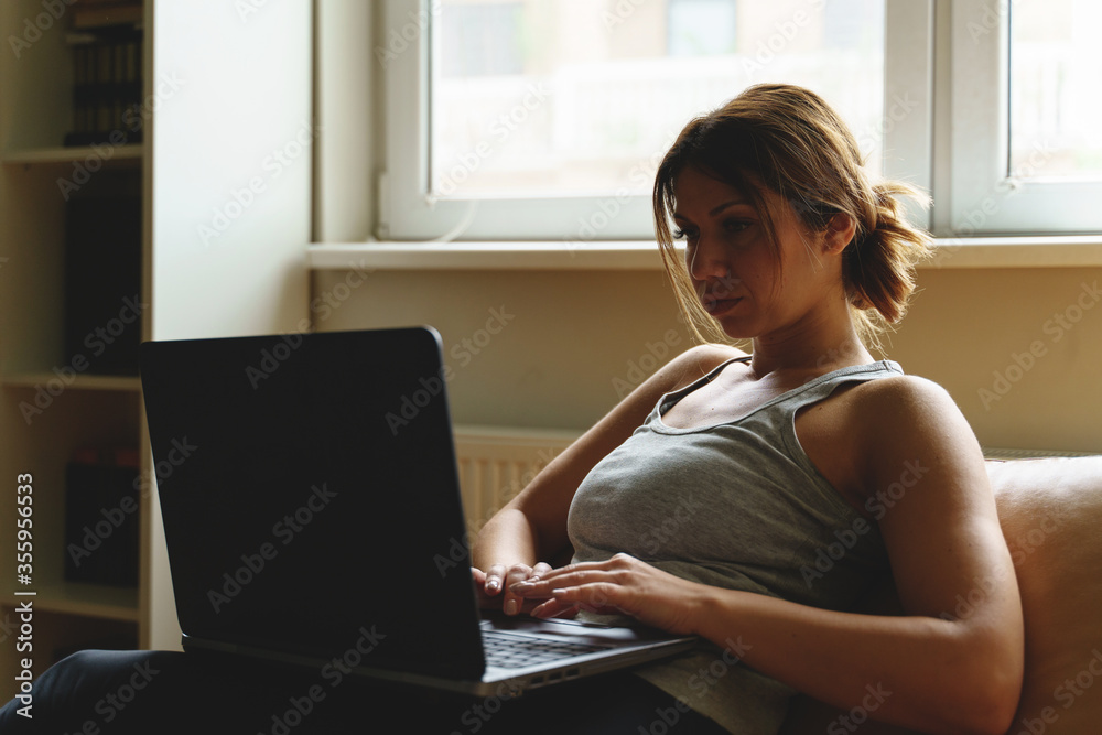 Young adult caucasian woman working on the laptop computer from home sitting on the sofa bed in day taping online female freelancer or shopping online efficiency and expertise making money concept Young adult caucasian woman working on the laptop computer from home sitting on the sofa bed in day taping online female freelancer or shopping online efficiency and expertise making money concept