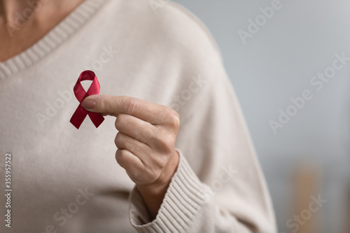 Close up of senior woman hold red ribbon breast cancer symbol support people patient with illness, middle-aged female volunteer keep AIDS HIV disease awareness, elderly healthcare, medicine concept photo
