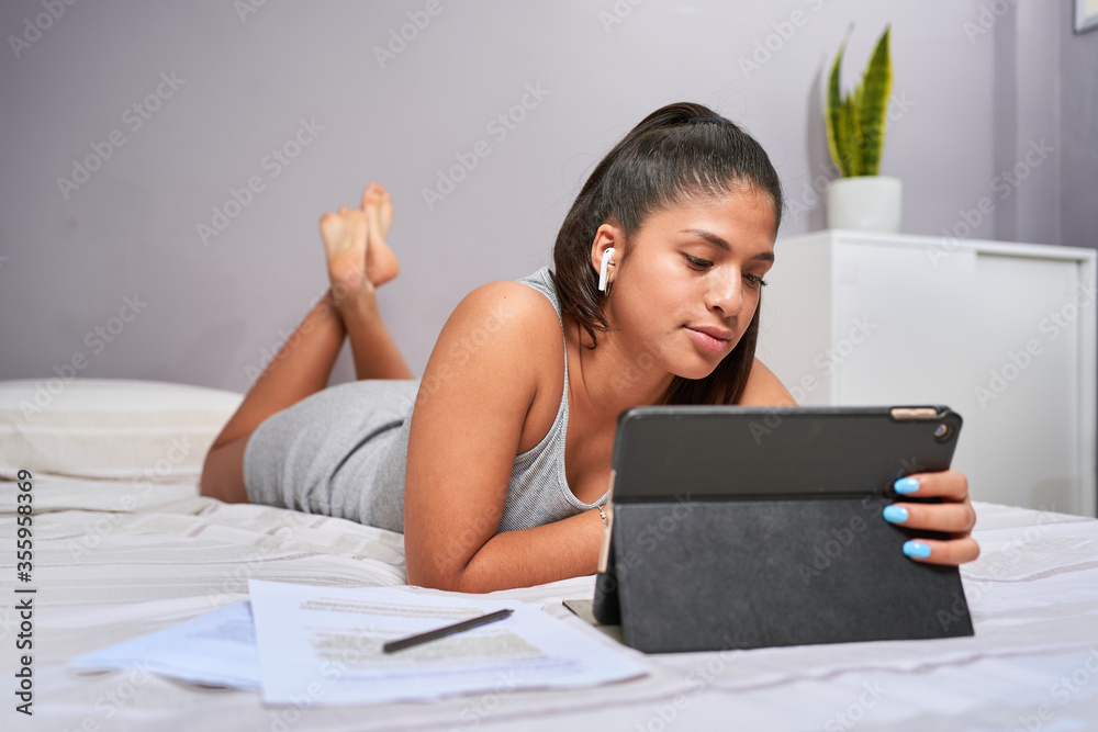 Young Latina studying and performing class assignments online with his computer from home for causes of coronavirus. Sitting at her table with leaves and pens. Videoconferencia con sus profesores. Young Latina studying and performing class assignments online with his computer from home for causes of coronavirus. Sitting at her table with leaves and pens. Videoconferencia con sus profesores.