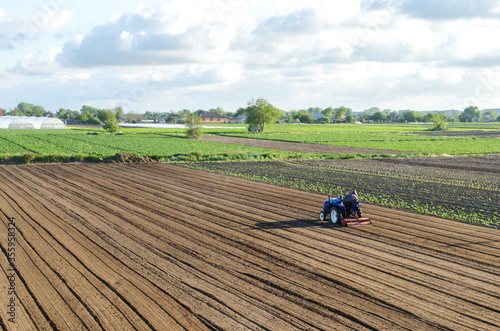 A tractor rides on a farm field. Loosening the surface, cultivating the land for further planting. Farmer on a tractor with milling machine loosens, grinds and mixes soil. Farming and agriculture. photo