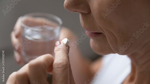 Close up of mature sick woman having antibiotic aspirin pill suffering from headache or migraine, ill senior female take daily dose of vitamin or supplement, medications, elderly healthcare concept photo