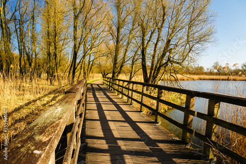 Wooden footbridge with a shadow from a low sun in a park in spring.
