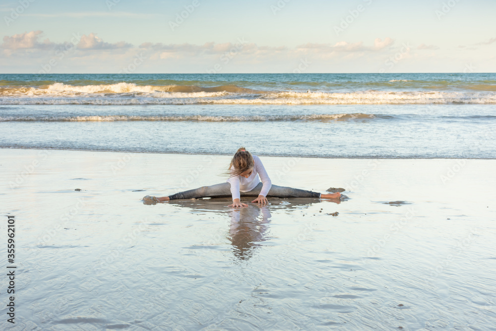 Child exercises and meditates on the beach sand