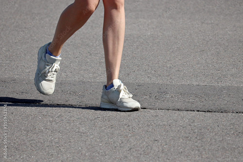 Slim girl running on a street, female legs in sneakers. Concept of workout, woman runner, slimming in summer season