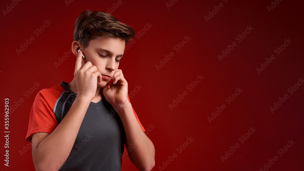 Concentration. A teenage boy engaged in sport, closing his eyes while listening to music via wireless earphones. Isolated on red background. Training, active lifestyle concept. Horizontal shot Concentration. A teenage boy engaged in sport, closing his eyes while listening to music via wireless earphones. Isolated on red background. Training, active lifestyle concept. Horizontal shot
