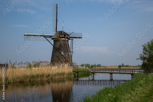Historic windmill at Kinderdijk, Netherlands hemmed in with reeds at the side of a canal crossed by a wooden foot bridge.
