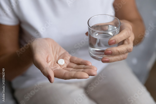 Close up of unhealthy elderly woman hold pill and glass of water feeling unwell sick at home, ill mature female take antibiotic aspirin drug, have headache or migraine, healthcare, medicine concept photo