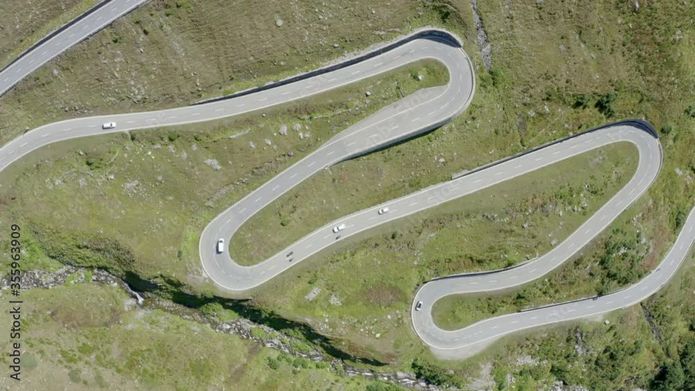 Aerial time lapse shot of vehicles on winding road during sunny day, drone flying over mountain road - Swiss Alps, Switzerland Aerial time lapse shot of vehicles on winding road during sunny day, drone flying over mountain road - Swiss Alps, Switzerland