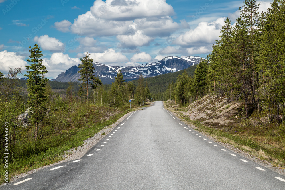 BD 805, a narrow, lonely road leading through the arctic wilderness of Lapland, Sweden, connecting Jokkmokk and Kvikkjokk. A rugged mountain range covered with snow is visible in the background. BD 805, a narrow, lonely road leading through the arctic wilderness of Lapland, Sweden, connecting Jokkmokk and Kvikkjokk. A rugged mountain range covered with snow is visible in the background.