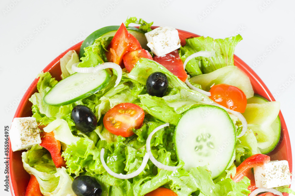 Vegetable salad on the plate, tomatoes, green salad, cheese, lemon and olive, other vegetables.