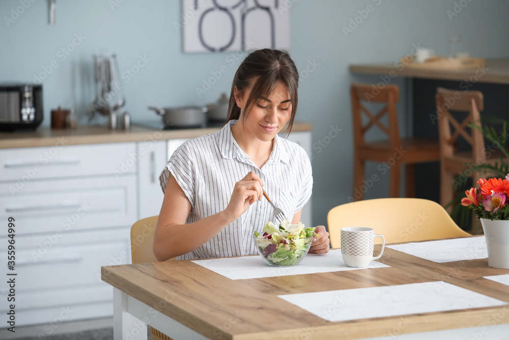 Beautiful young woman eating healthy salad in kitchen Beautiful young woman eating healthy salad in kitchen