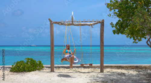 CLOSE UP: Joyful woman swings on the scenic swings on a tropical sandy beach