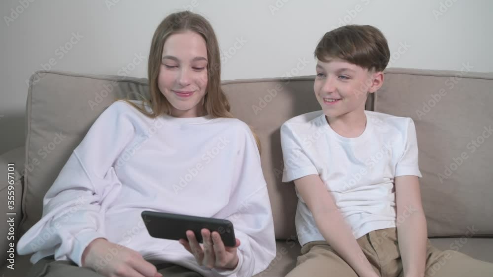 Children with a phone in their hands at home, two children watching cartoons Children with a phone in their hands at home, two children watching cartoons