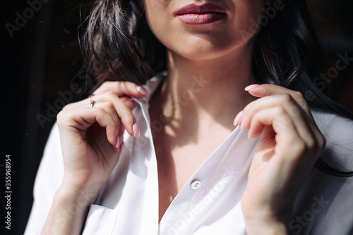 Luxurious lips with lipstick of a beautiful brunette girl close-up, female hands hold the collar of a white blouse