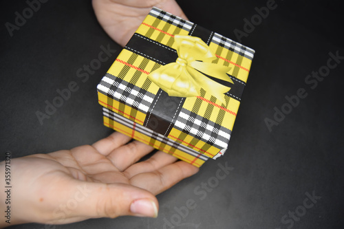 Young woman holding Multicolored yellow gift box on black background, Young girl yellow gift box isolated on black background