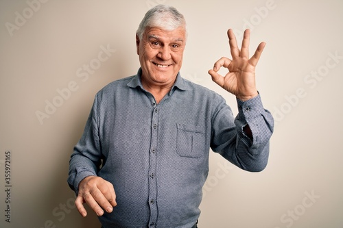 Senior handsome hoary man wearing casual shirt standing over isolated white background smiling positive doing ok sign with hand and fingers. Successful expression.