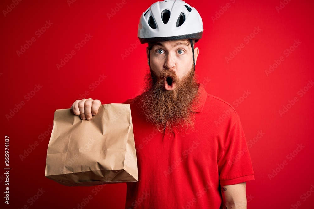 Redhead Irish delivery man with beard wearing bike helmet and holding takeaway paper bag scared in shock with a surprise face, afraid and excited with fear expression Redhead Irish delivery man with beard wearing bike helmet and holding takeaway paper bag scared in shock with a surprise face, afraid and excited with fear expression
