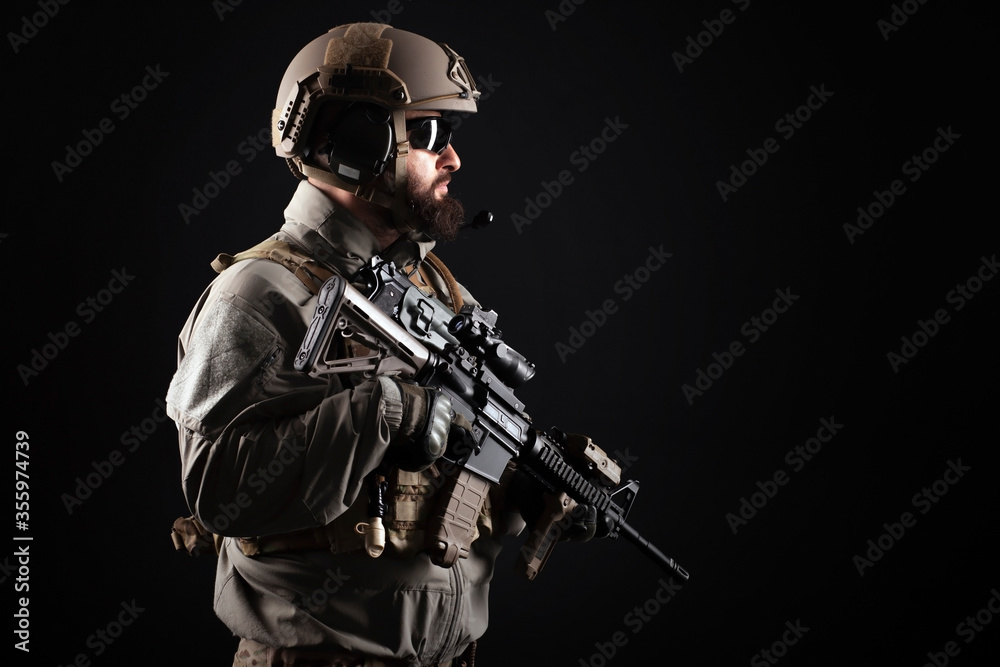American special forces against a dark background, a soldier in military equipment holds weapons and looks at the copy space
