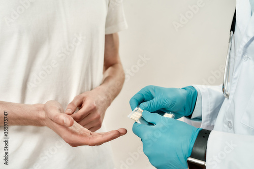 Close up of a doctor in blue sterile gloves giving pills to patient while standing against grey background. Healthcare and medicine. Focus on hands