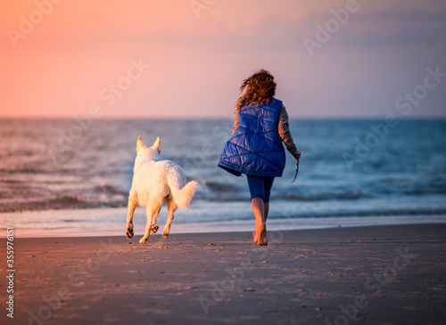 Dziewczyna i biały pies spacerują nad morzem