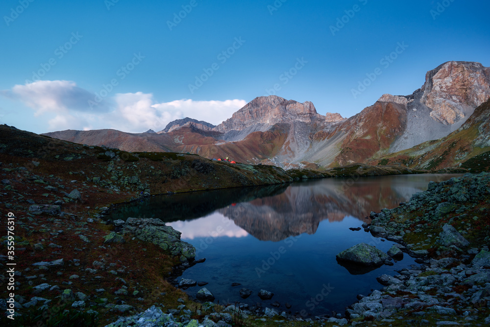 Beautiful mountains at sunset in clouds, gold alpine field, lakes and mountain ranges, travel and mountain life. Campground by the lake
