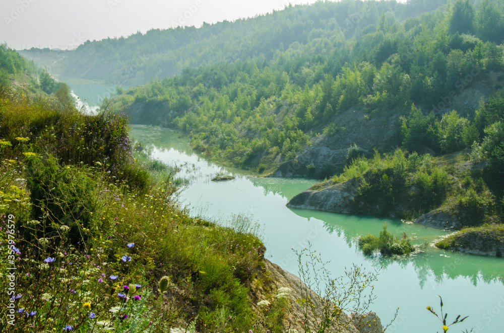 Turquoise water of the river flowing into the gorge at the foot of chalk hills overgrown with deep green plants and flowers
