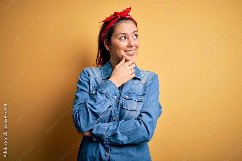 Young beautiful brunette woman wearing casual denim shirt and hair handkerchief with hand on chin thinking about question, pensive expression. Smiling with thoughtful face. Doubt concept. Young beautiful brunette woman wearing casual denim shirt and hair handkerchief with hand on chin thinking about question, pensive expression. Smiling with thoughtful face. Doubt concept.