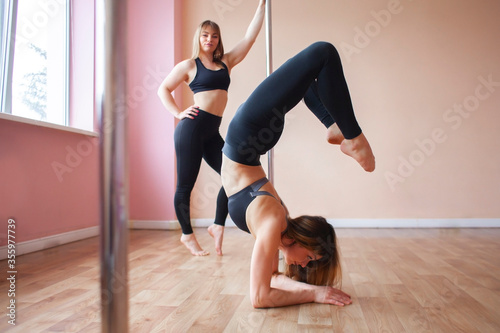 pole dance team, two girls gymnasts train together, girlfriends do trick on the pylon