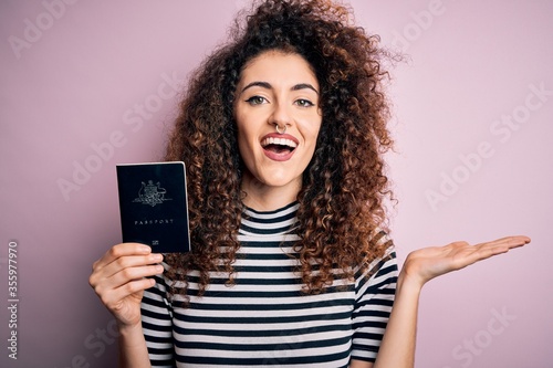 Beautiful tourist woman with curly hair and piercing holding australia australian passport id very happy and excited, winner expression celebrating victory screaming with big smile and raised hands