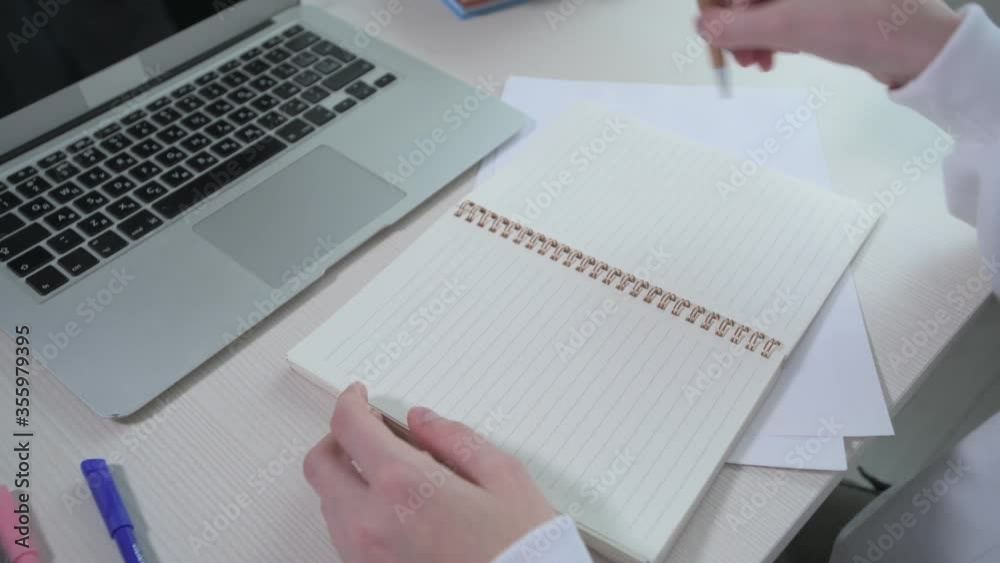 On the table in front of the girl is a blank notebook and a laptop. On the table in front of the girl is a blank notebook and a laptop.