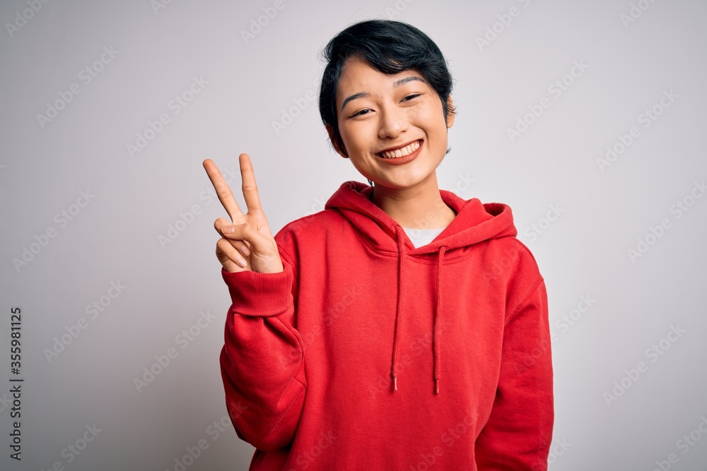 Young beautiful asian girl wearing casual sweatshirt with hoodie over white background showing and pointing up with fingers number two while smiling confident and happy. Young beautiful asian girl wearing casual sweatshirt with hoodie over white background showing and pointing up with fingers number two while smiling confident and happy.