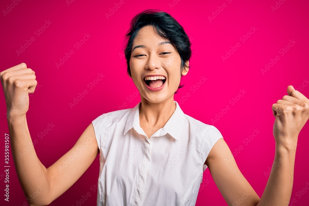 Young beautiful asian girl wearing casual summer shirt standing over isolated pink background celebrating surprised and amazed for success with arms raised and open eyes. Winner concept. Young beautiful asian girl wearing casual summer shirt standing over isolated pink background celebrating surprised and amazed for success with arms raised and open eyes. Winner concept.