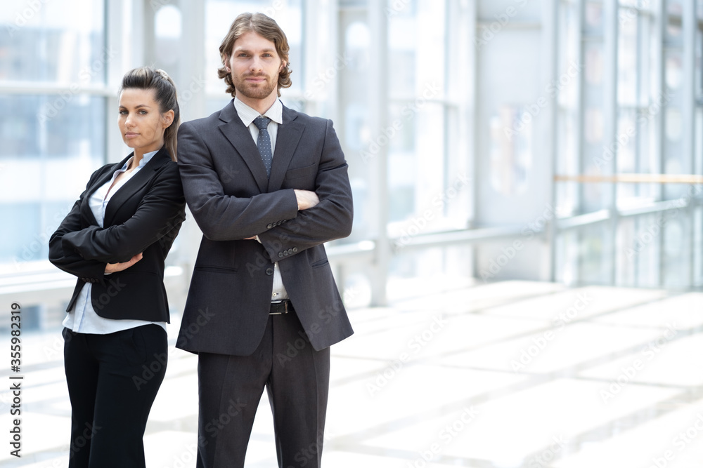 Professional business man and woman standing back to back in the office looking at the camera Professional business man and woman standing back to back in the office looking at the camera