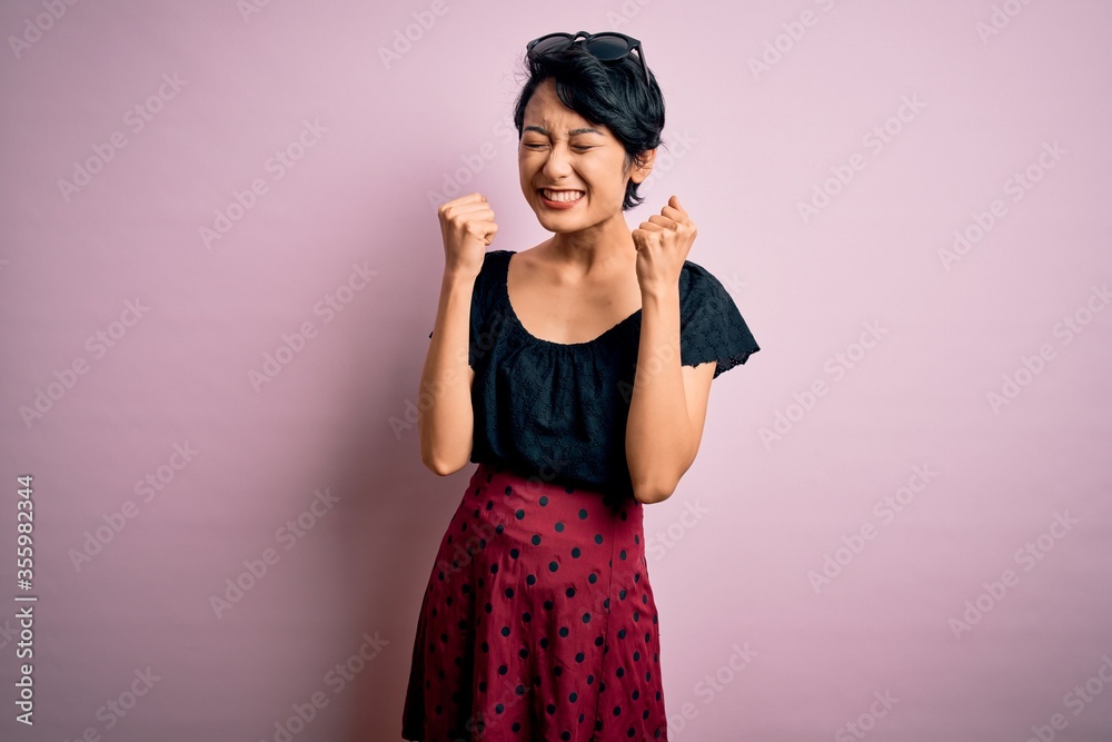 Young beautiful asian girl wearing casual dress standing over isolated pink background excited for success with arms raised and eyes closed celebrating victory smiling. Winner concept. Young beautiful asian girl wearing casual dress standing over isolated pink background excited for success with arms raised and eyes closed celebrating victory smiling. Winner concept.