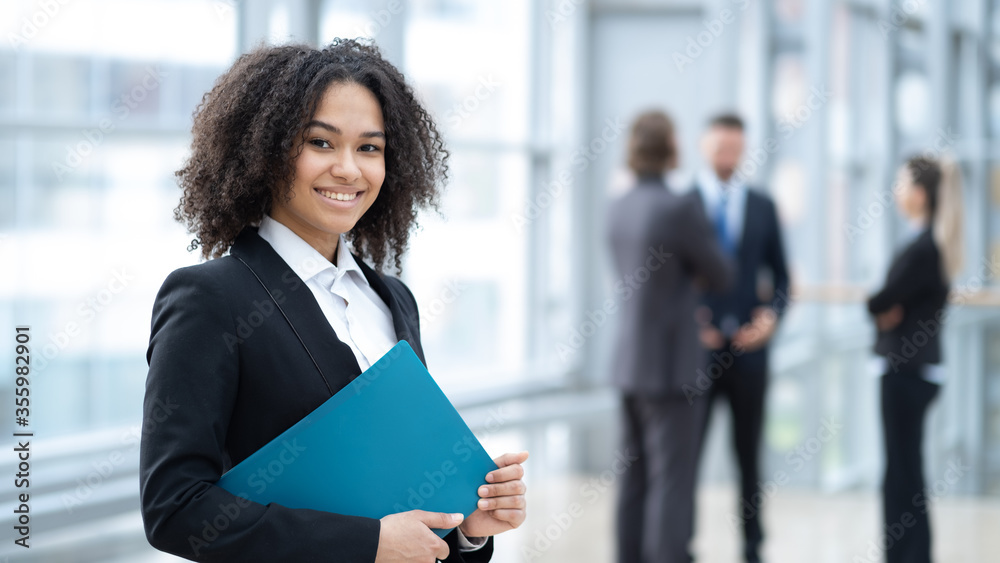 African business woman holding clipboard with colleague on background African business woman holding clipboard with colleague on background