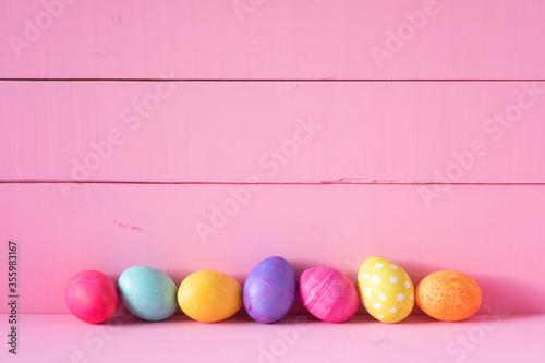 Colorful Easter Eggs in a Row on a Table and against a Bright Pink Board Wall Background with copy space. Horizontal and wide with side view