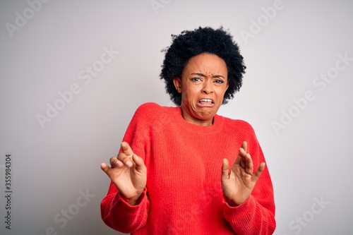 Young beautiful African American afro woman with curly hair wearing red casual sweater disgusted expression, displeased and fearful doing disgust face because aversion reaction.