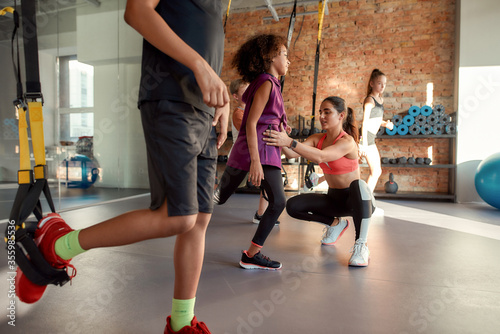 Portrait of teenage kids training using fitness straps in gym while female trainer helping them. Sport, healthy lifestyle, physical education concept