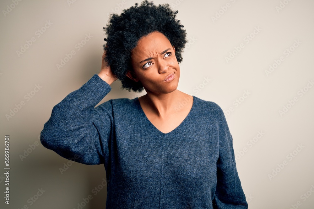 Young beautiful African American afro woman with curly hair wearing casual sweater confuse and wondering about question. Uncertain with doubt, thinking with hand on head. Pensive concept. Young beautiful African American afro woman with curly hair wearing casual sweater confuse and wondering about question. Uncertain with doubt, thinking with hand on head. Pensive concept.