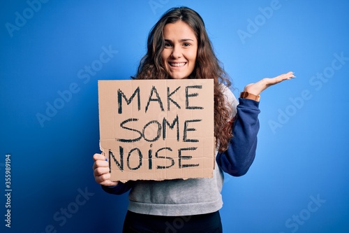 Tableau sur toile Beautiful activist woman holding banner with make some noise message over blue b