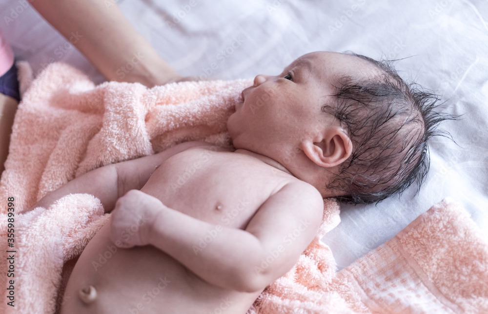newborn baby lying in a bath towel on the bed with mother hands holding towel newborn baby lying in a bath towel on the bed with mother hands holding towel