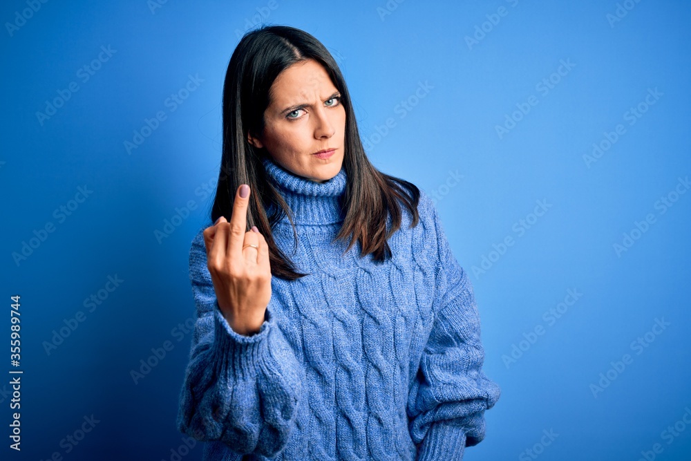 Young brunette woman with blue eyes wearing casual turtleneck sweater Showing middle finger, impolite and rude fuck off expression Young brunette woman with blue eyes wearing casual turtleneck sweater Showing middle finger, impolite and rude fuck off expression