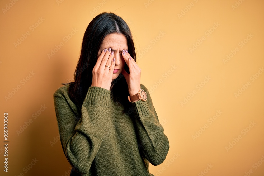 Φωτογραφία Young brunette woman with blue eyes wearing green casual sweater over yellow background rubbing eyes for fatigue and headache, sleepy and tired expression