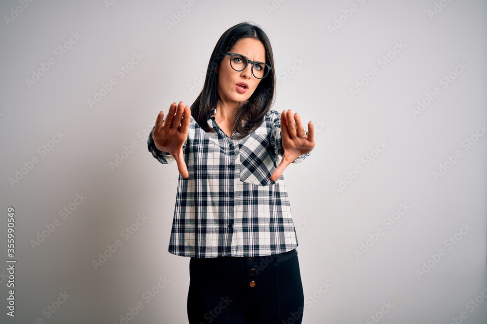 Young brunette woman with blue eyes wearing casual shirt and glasses over white background doing stop gesture with hands palms, angry and frustration expression Young brunette woman with blue eyes wearing casual shirt and glasses over white background doing stop gesture with hands palms, angry and frustration expression